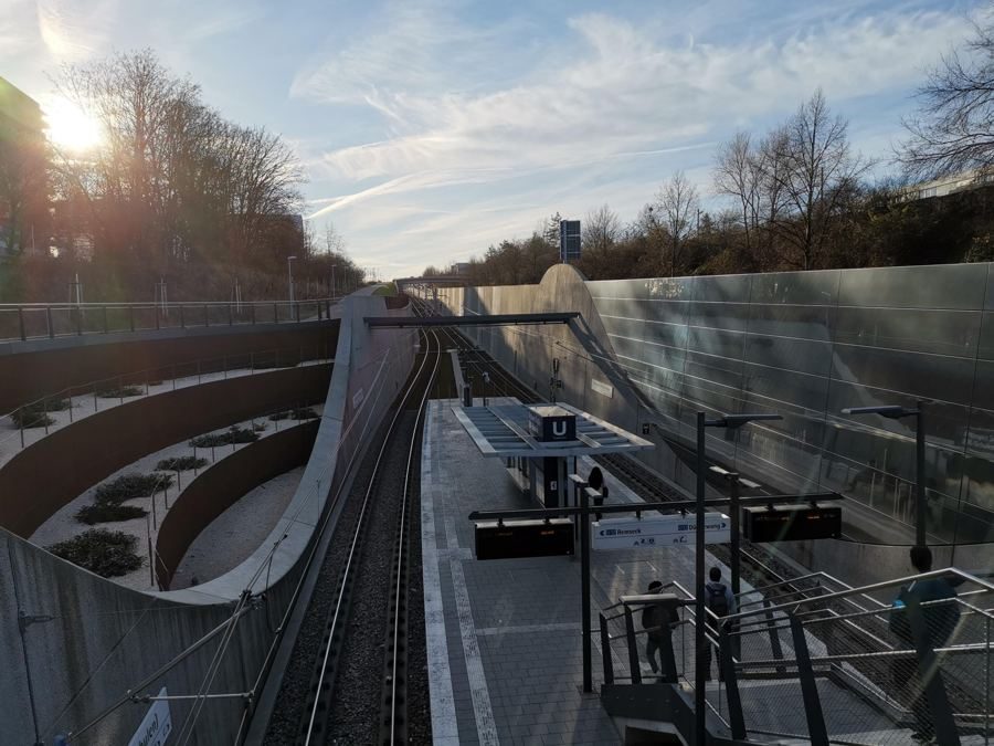 Blick auf eine tiefergelegte Schienenstrecke mit Haltestelle und beidseitigen Schallschutzwänden